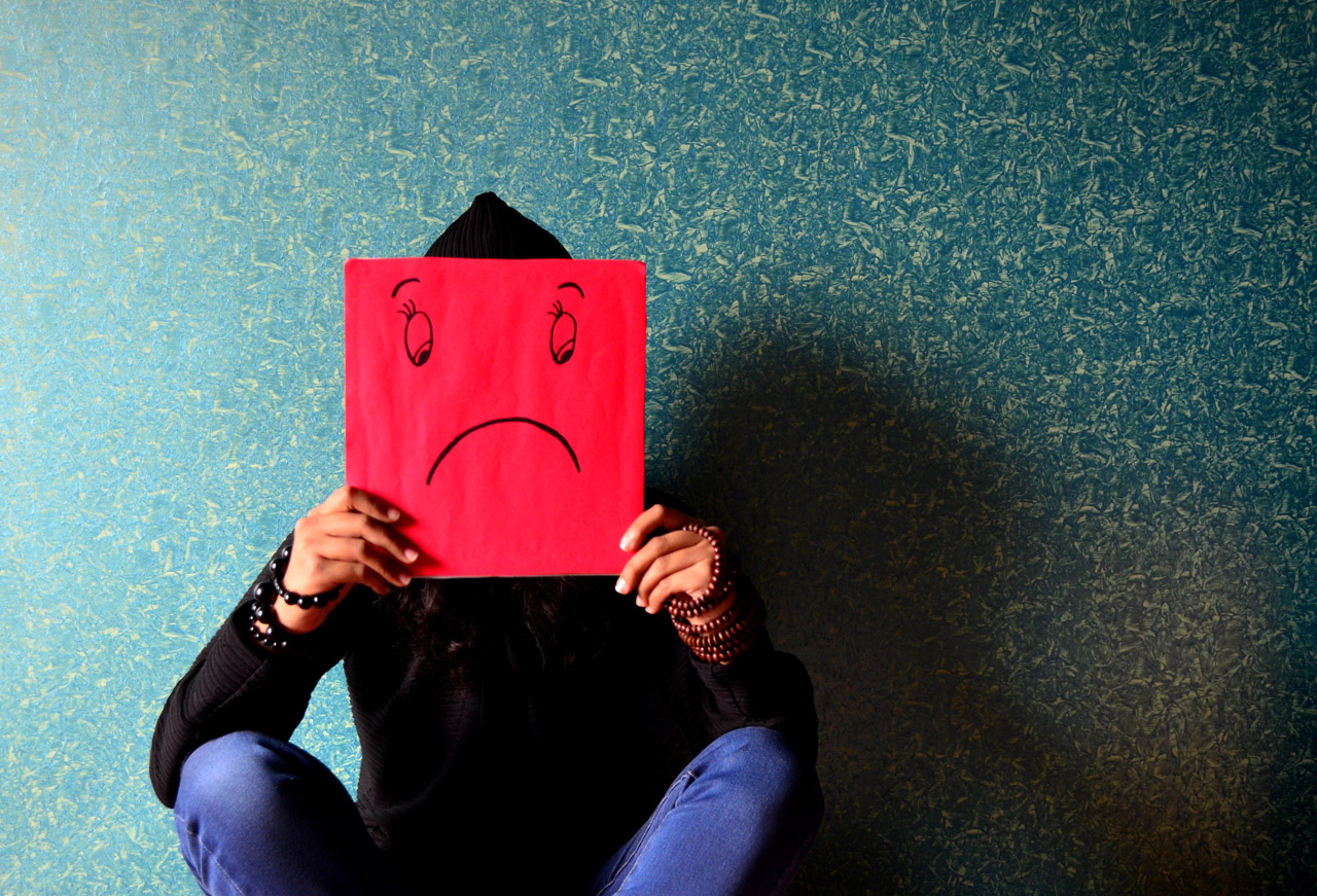 A seated man holding up a sad face sign